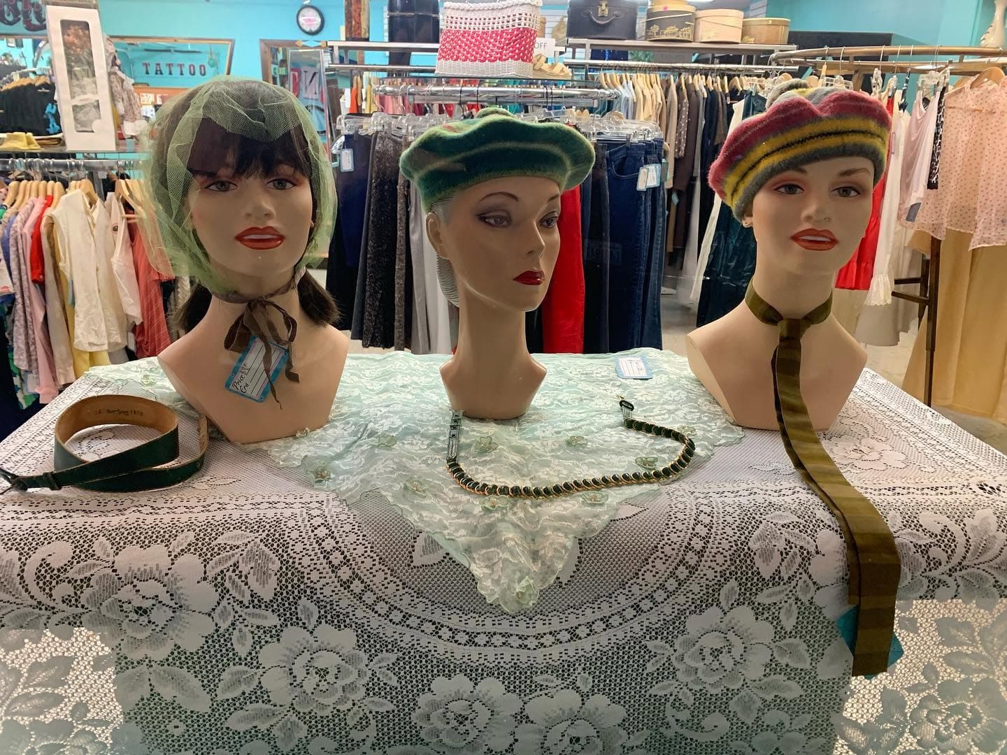 Three mannequin heads in vintage hats with jewelry laid on a lace-covered table