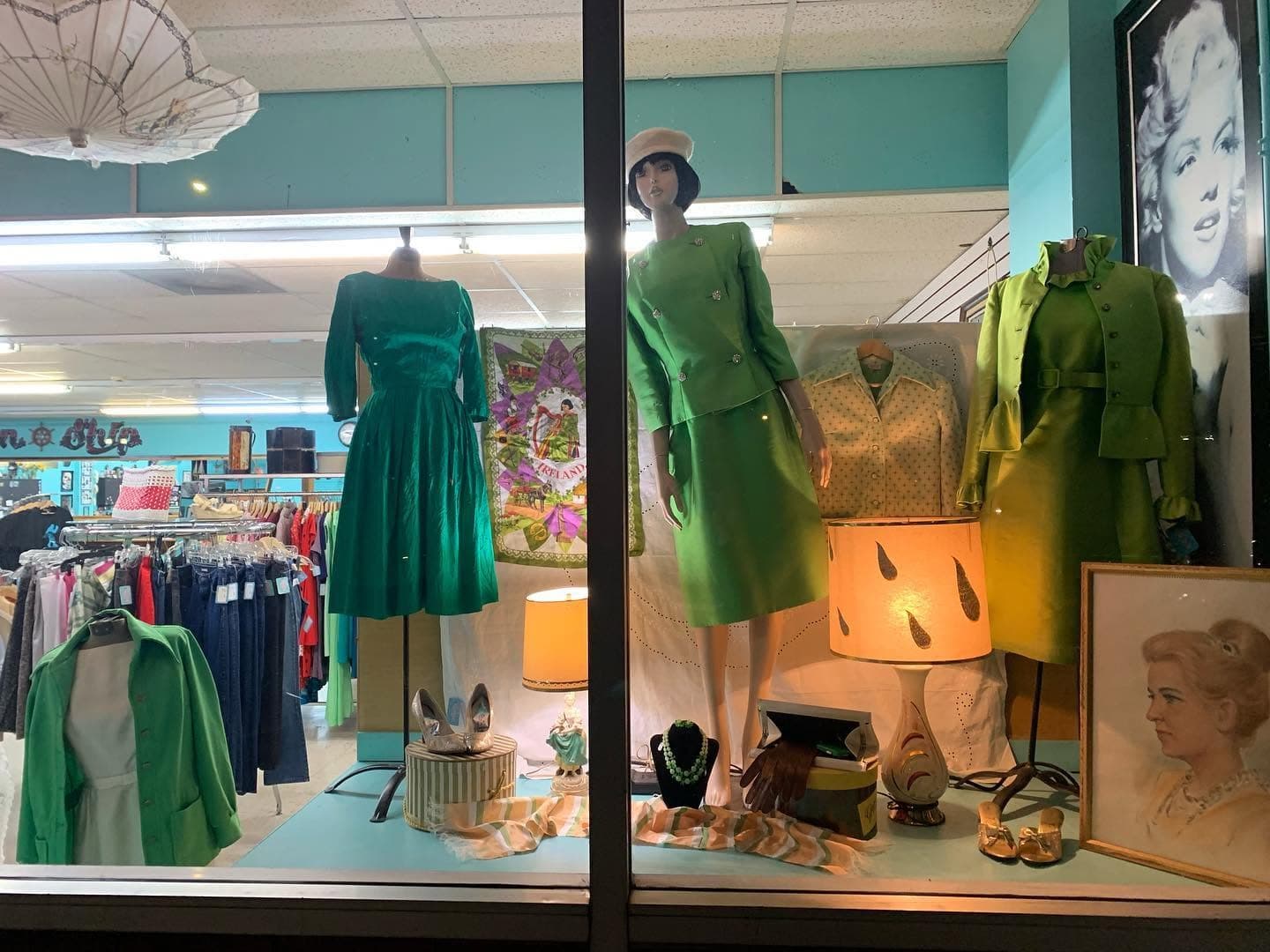 Vintage window display with green dresses, retro lamps and a framed pin-up portrait