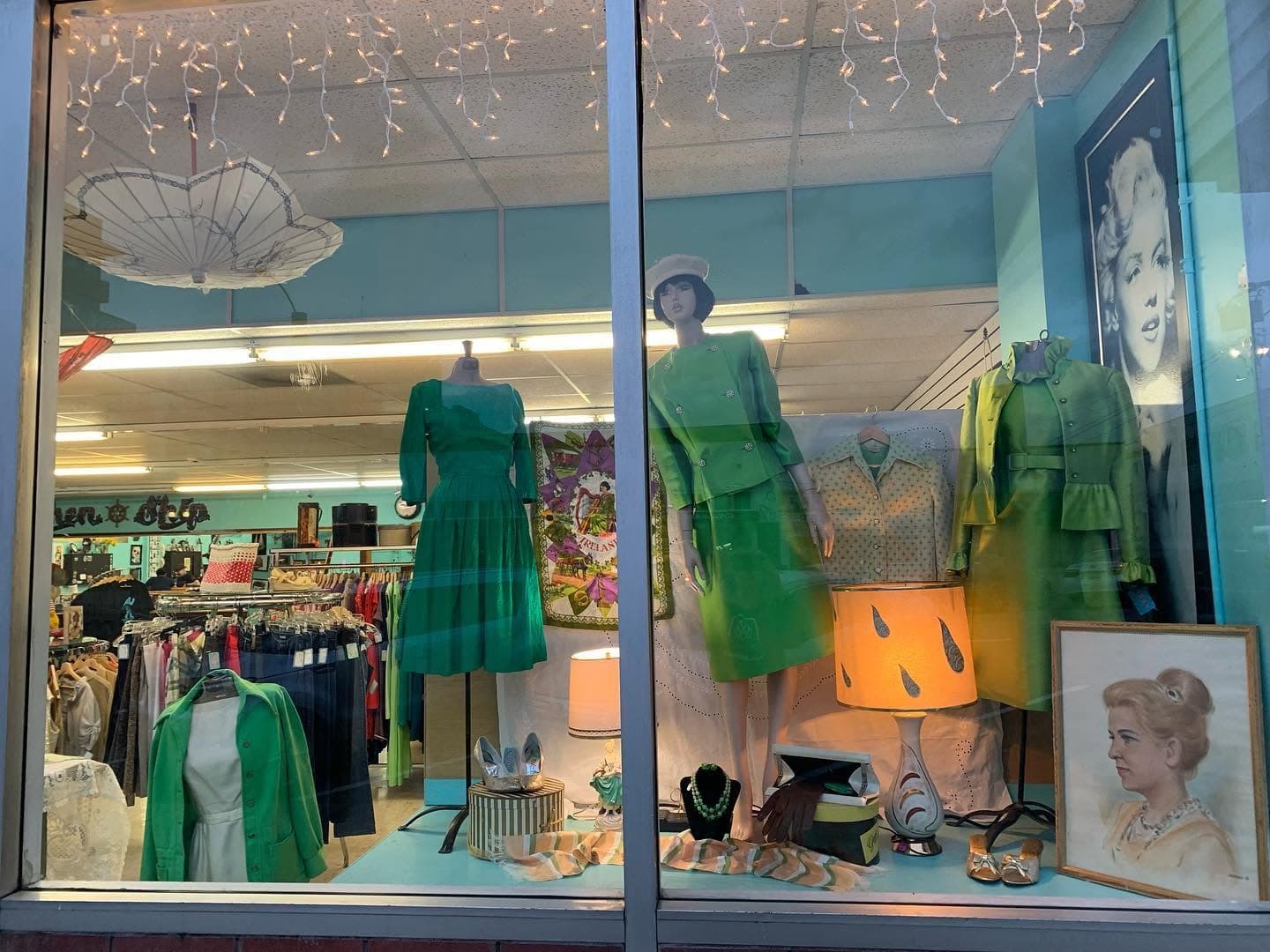 Window display of vintage dresses on mannequins against the shop’s aqua walls