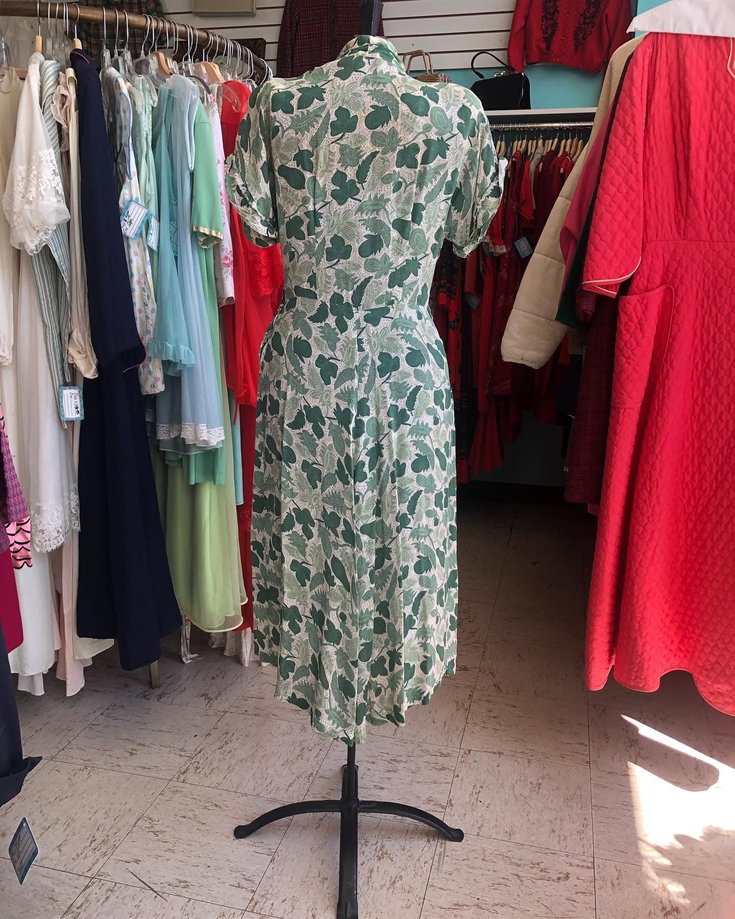A printed vintage dress on a stand in front of a dense clothing rack